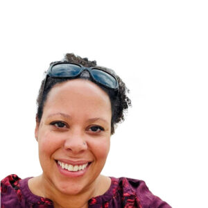 Rhi Wasmann, a smiling woman with curly dark hair and sunglasses worn on her head, looks at the camera against a plain white backdrop.