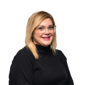 Kayla Lowery, with shoulder-length blonde hair, smiles brightly in a black turtleneck sweater and clear-rimmed glasses.